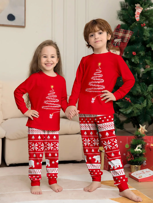 Two children wearing red Christmas-themed pajamas in a living room with a decorated tree.