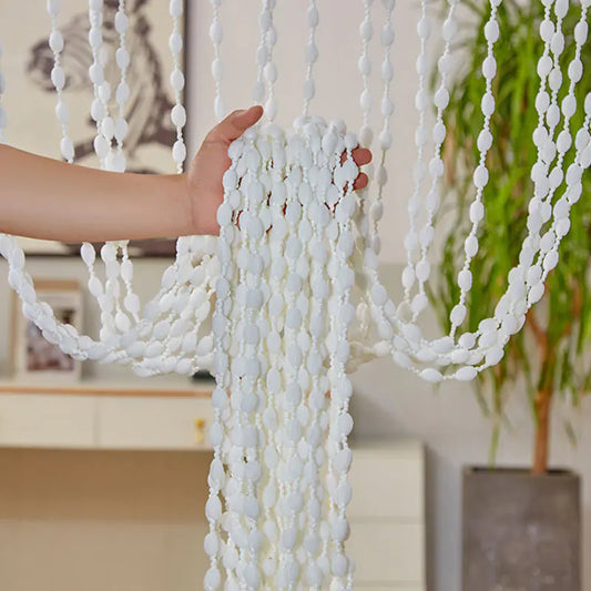 White beaded curtain with a hand holding it, indoor setting with decor elements.