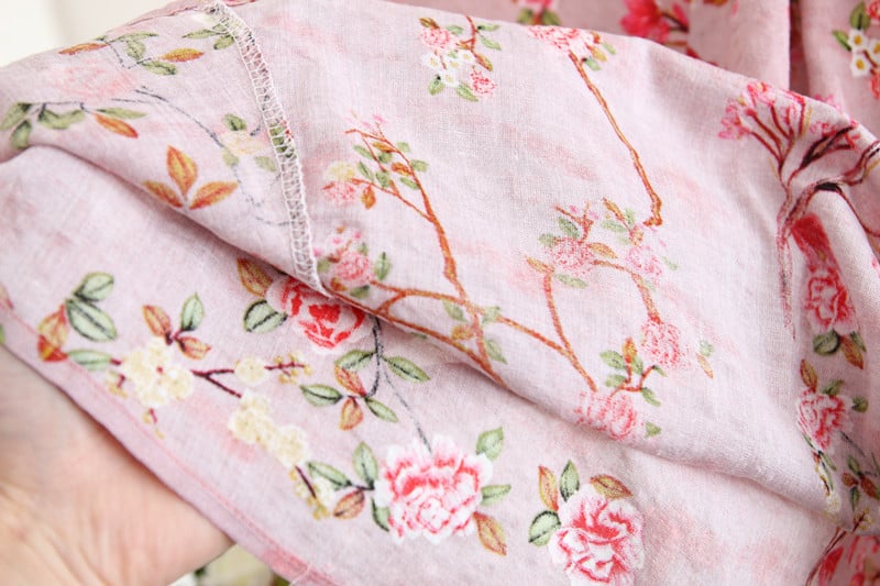 Floral patterned fabric with pink flowers and green leaves on a light pink background.