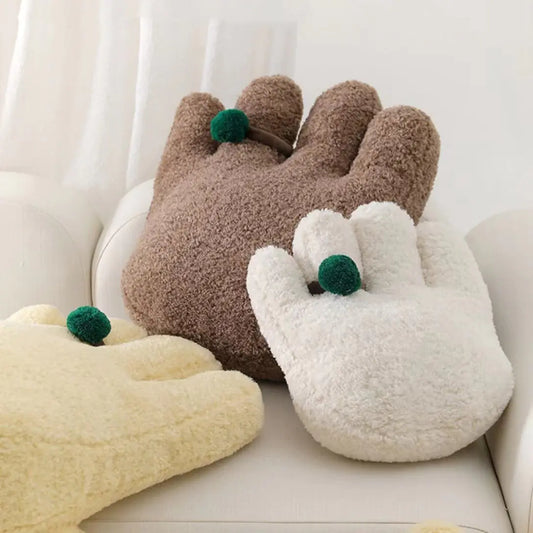 Three plush paw-shaped cushions in brown, white, and beige on a light-colored surface.