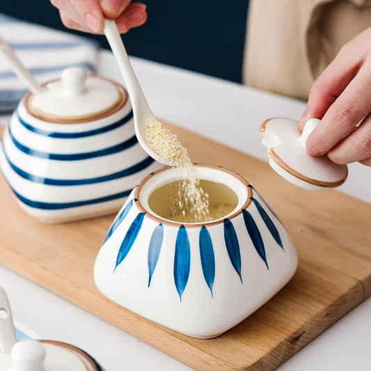 Person adding sugar to a japanese ceramic spice jar with blue patterns on a wooden board.