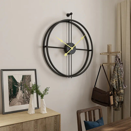 Large round wall clock with yellow hands on a neutral wall, with a wooden side table and decorative items.
