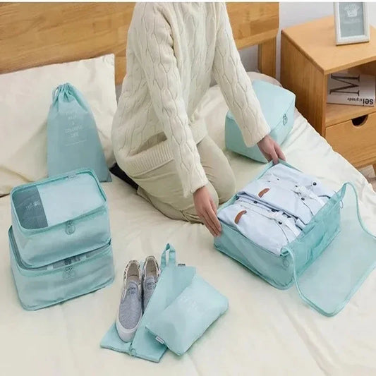 Person packing clothes into green travel bags on a bed