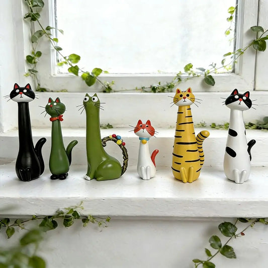 Set of colorful cat-shaped figurines on a white surface with a window and greenery in the background.