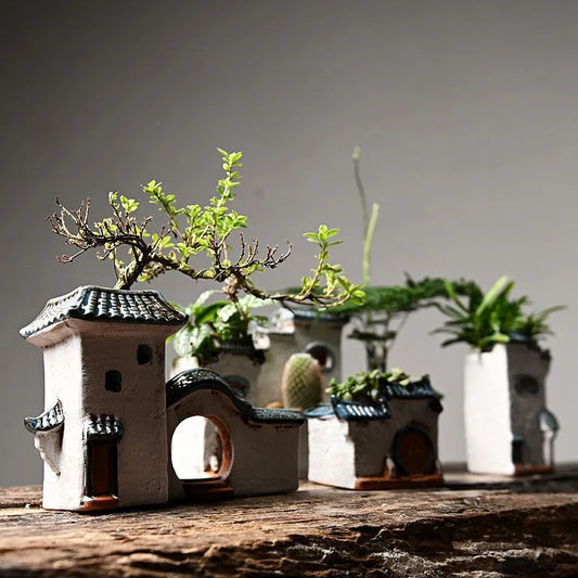 Small ceramic planter buildings with plants on a wooden surface