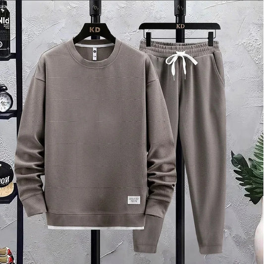 Gray sweatshirt and pants set on hangers against a gray wall.