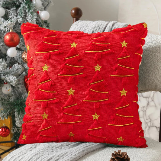 Red pillow with gold tree patterns and stars on a couch next to a Christmas tree.