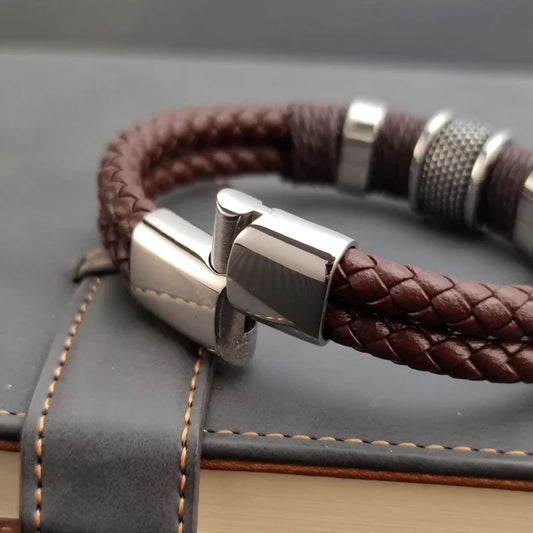 Brown braided leather bracelet with silver clasp on a textured surface