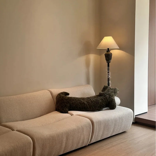 dachshund-shaped cushion on a Beige sofa with a decorative pillow in a room with a lamp and neutral walls.