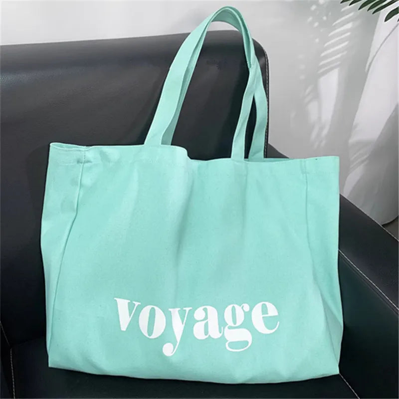 Mint green tote bag with 'Voyage' text on a black surface