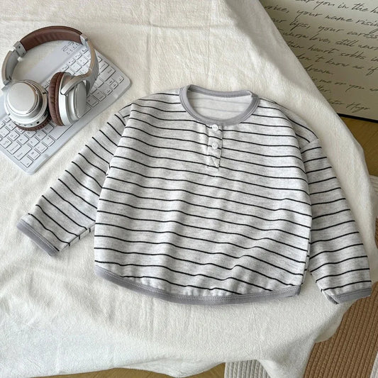 Striped baby shirt on a white surface with headphones and a keyboard.