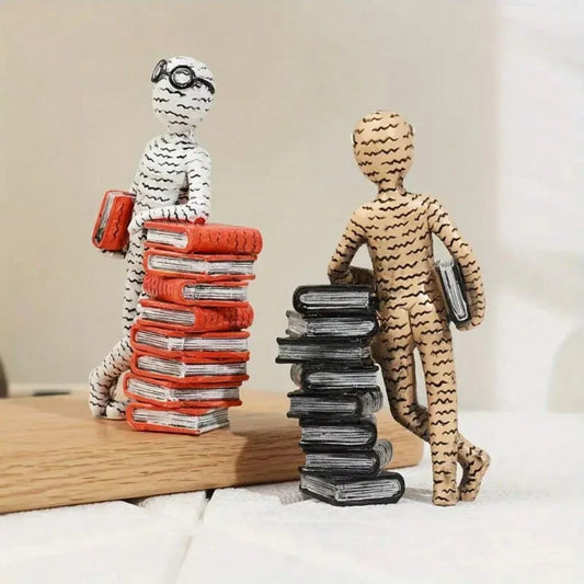Two figurines, one with a stack of books and the other with a suitcase, on a wooden surface.