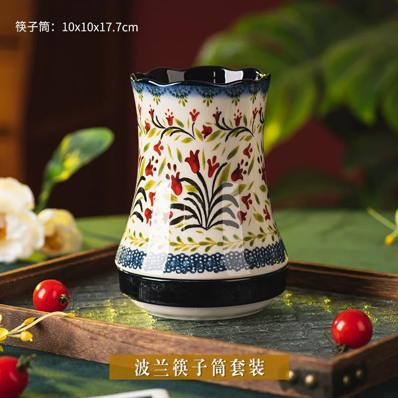 Decorative ceramic utensil holder with floral patterns on a wooden tray with fruits and leaves.