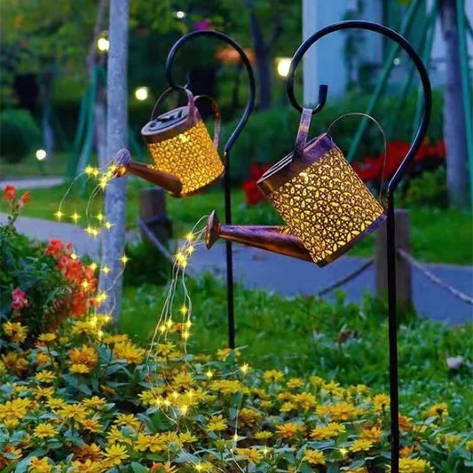 Decorative solar lights shaped like watering cans in a garden setting with flowers and string lights.