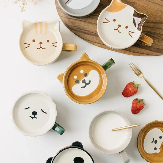 Cat-shaped ceramic mugs and bowls on a white surface with strawberries and a fork.