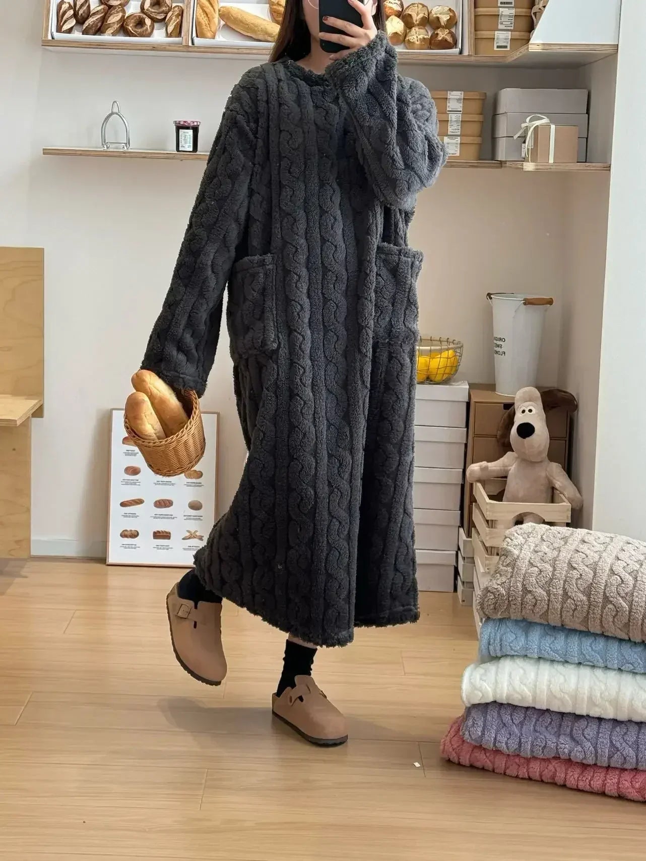 Person wearing a long dark gray cable knit sweater in a room with shelves and folded sweaters.