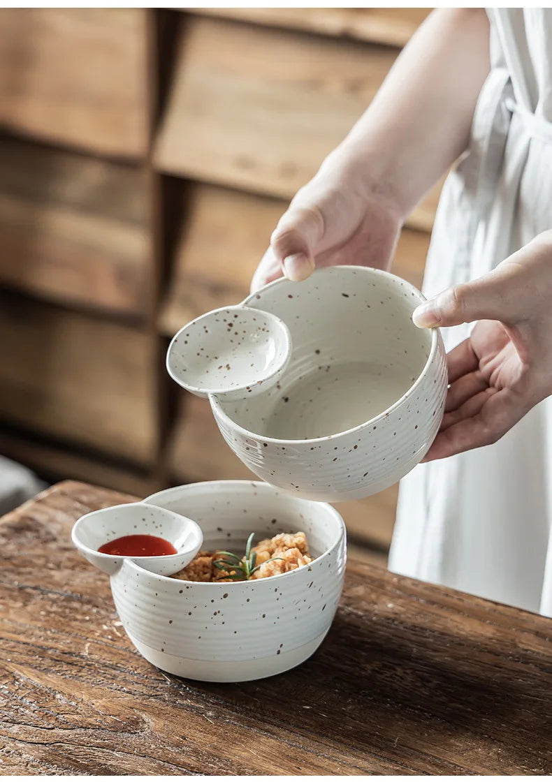 Person holding a ceramic bowl with another bowl on a wooden surface