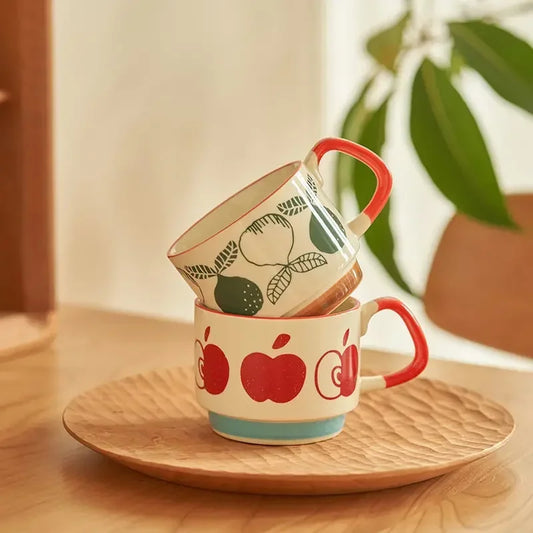 Two ceramic mugs with apple designs on a wooden plate.