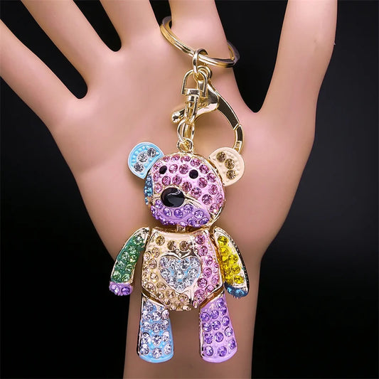 Colorful teddy bear keychain held in a hand against a black background