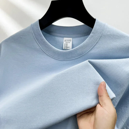 Light blue t-shirt held by a hand on a plain background