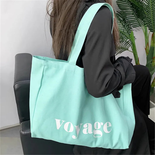 Person holding a light blue tote bag with 'Voyage' printed on it.