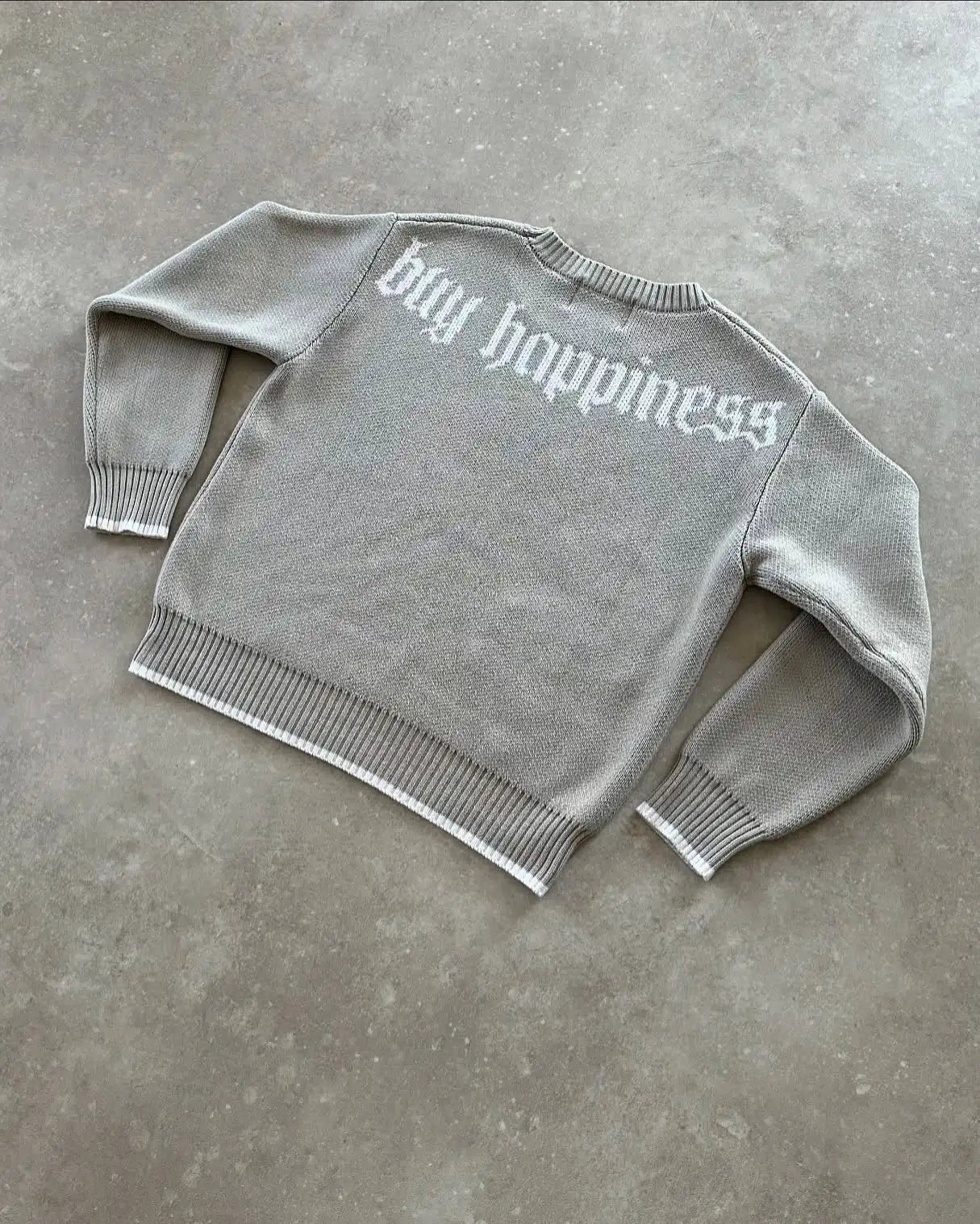 Gray sweater with 'big happiness' text on a concrete surface