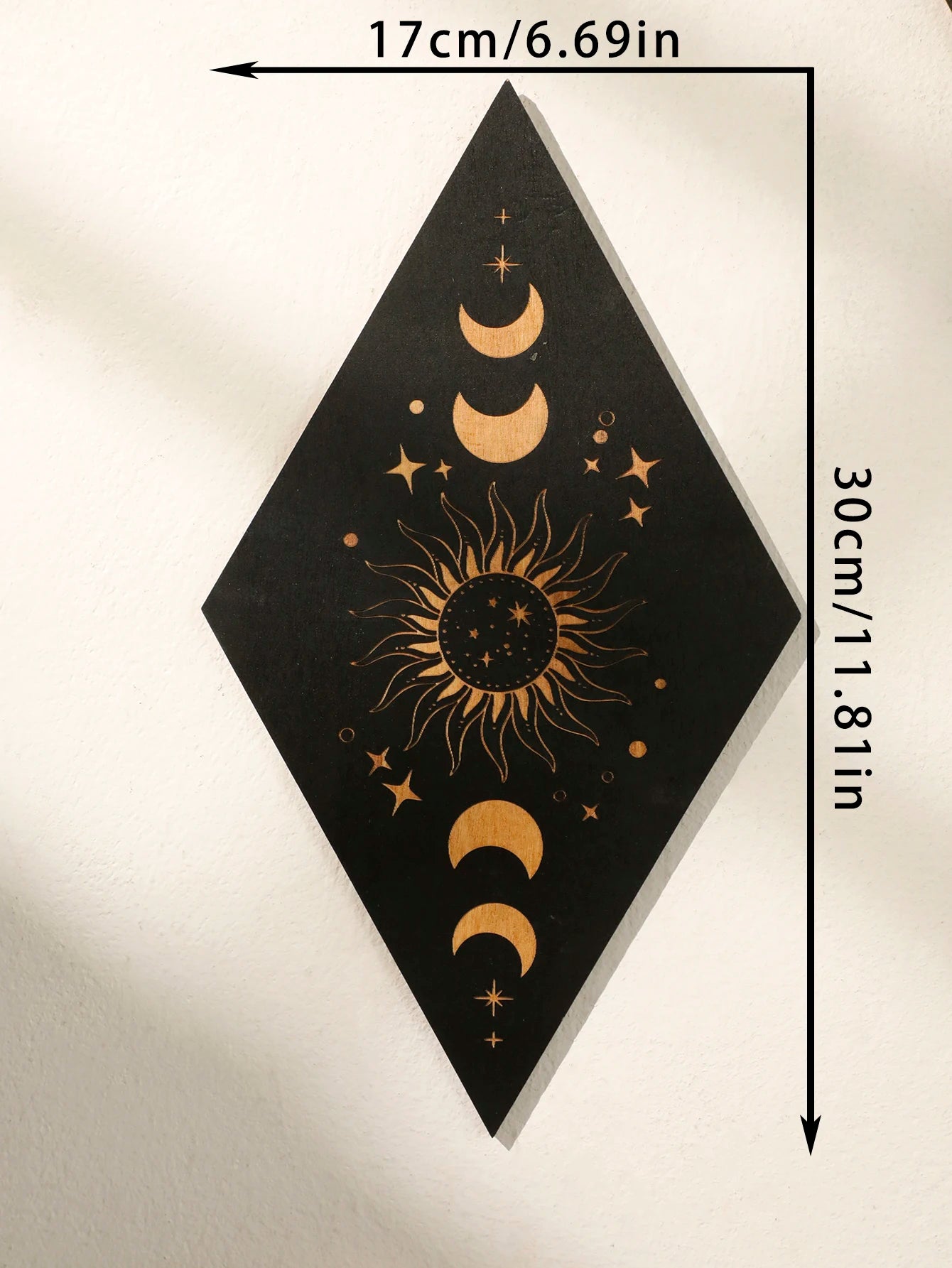 A black diamond-shaped wall art piece with gold celestial designs including a central sun, crescent moons, and stars, shown on a light wall with dimension arrows and text indicating 17cm by 30cm.
