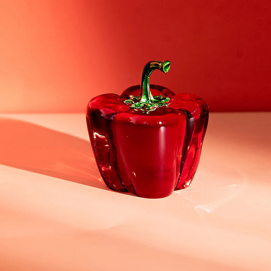 Red glass pepper on a peach-colored surface with a red background
