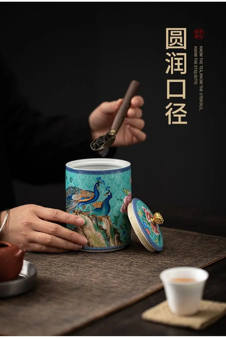 Person holding a decorative tea canister with peacock design on a table.