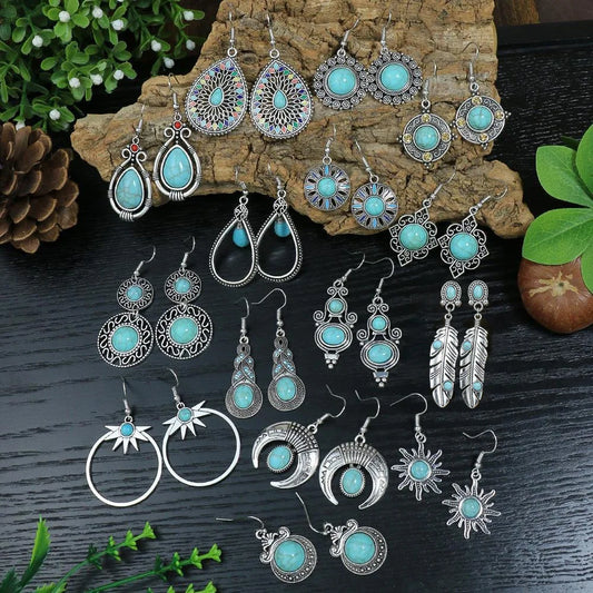 Collection of turquoise and silver earrings on a wooden and dark surface with greenery.
