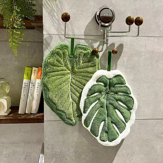 Leaf-shaped green towels hanging on a rack against a gray tiled wall.