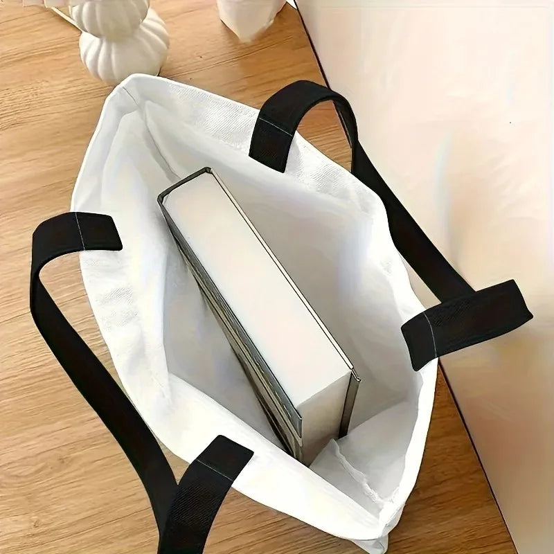 White tote bag with black straps containing a white box on a wooden surface.