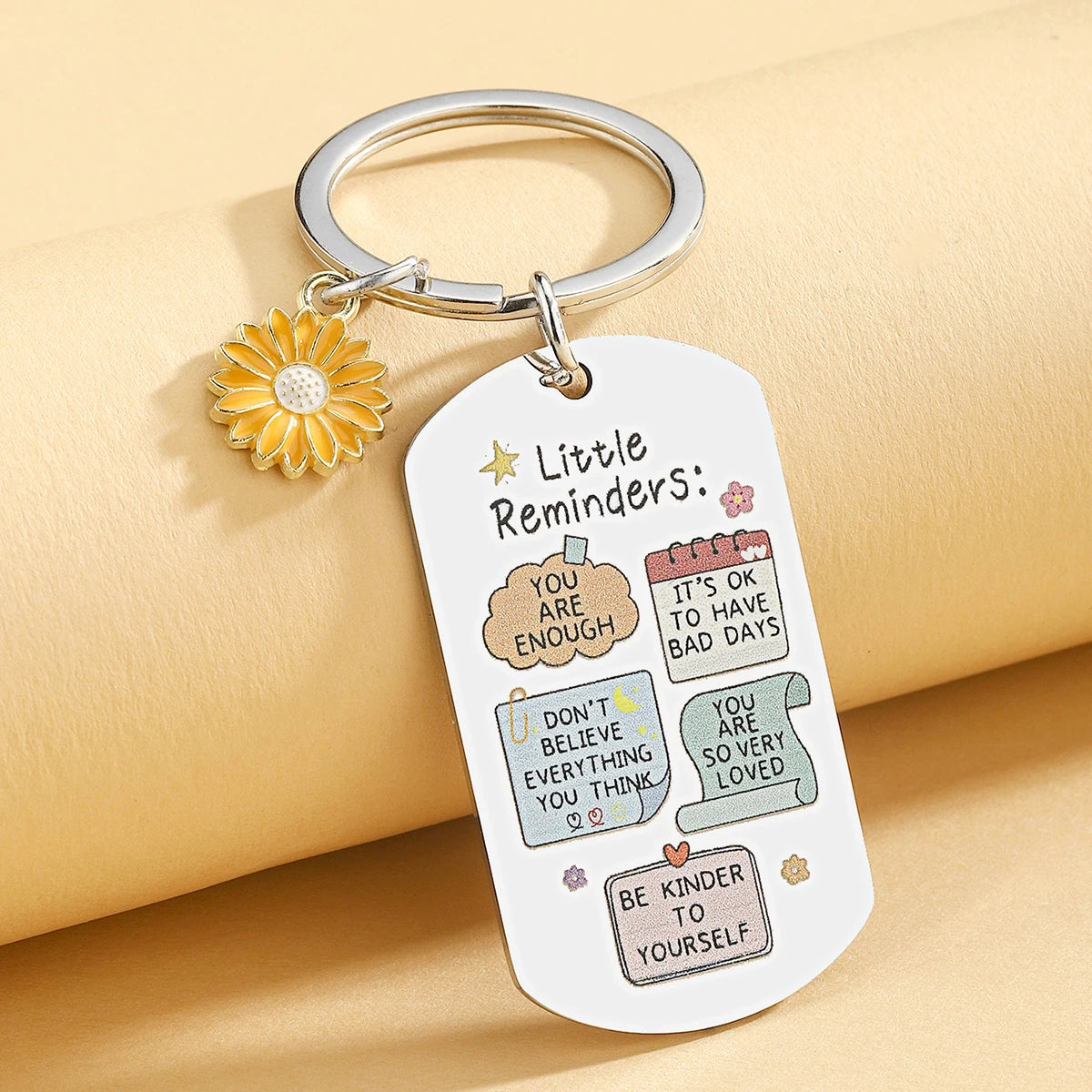 Keychain with motivational phrases and a sunflower charm on a beige background