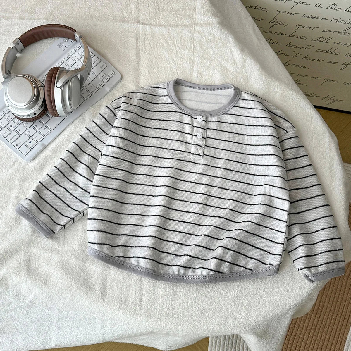 Striped baby shirt on a white surface with headphones and a keyboard.