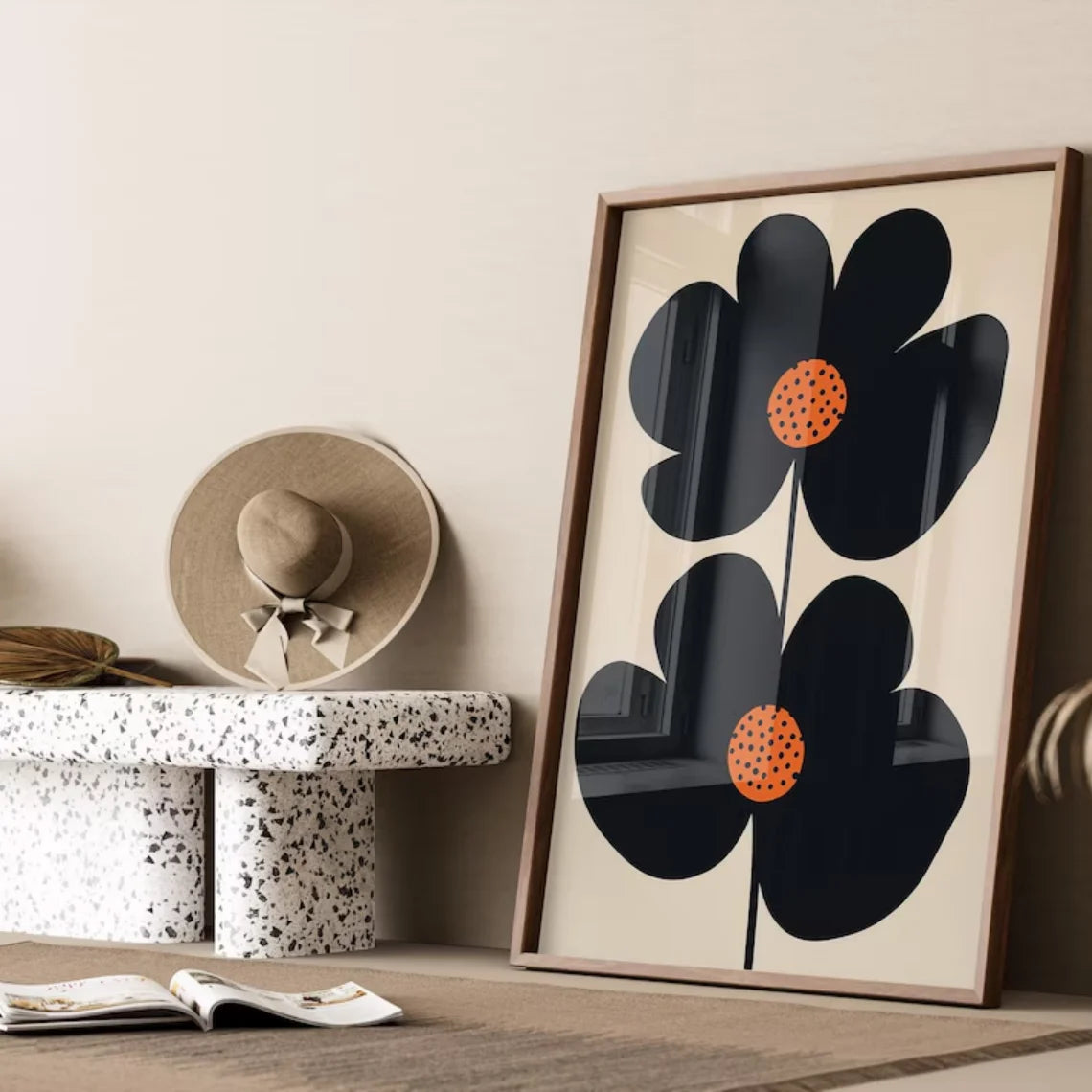 Framed abstract floral artwork with black and orange flowers on a beige background, placed on a wooden surface.