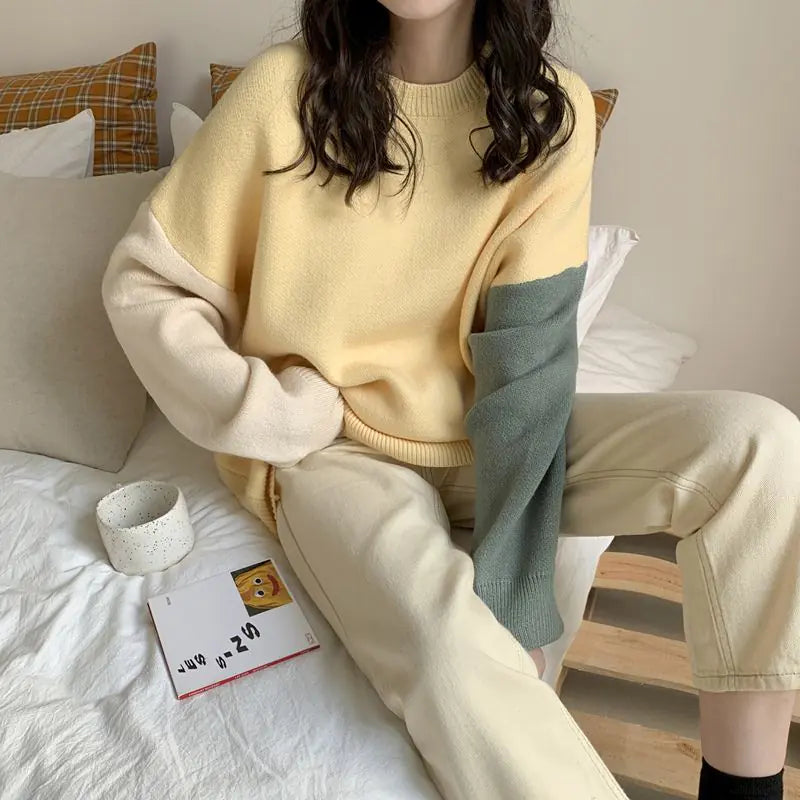 Person wearing a yellow and beige sweater sitting on a bed with pillows and a small table.