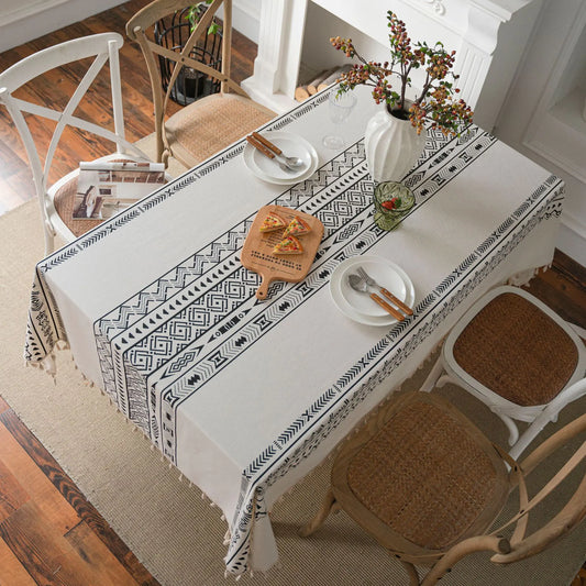 Dining table with a patterned tablecloth, chairs, and a vase with flowers.