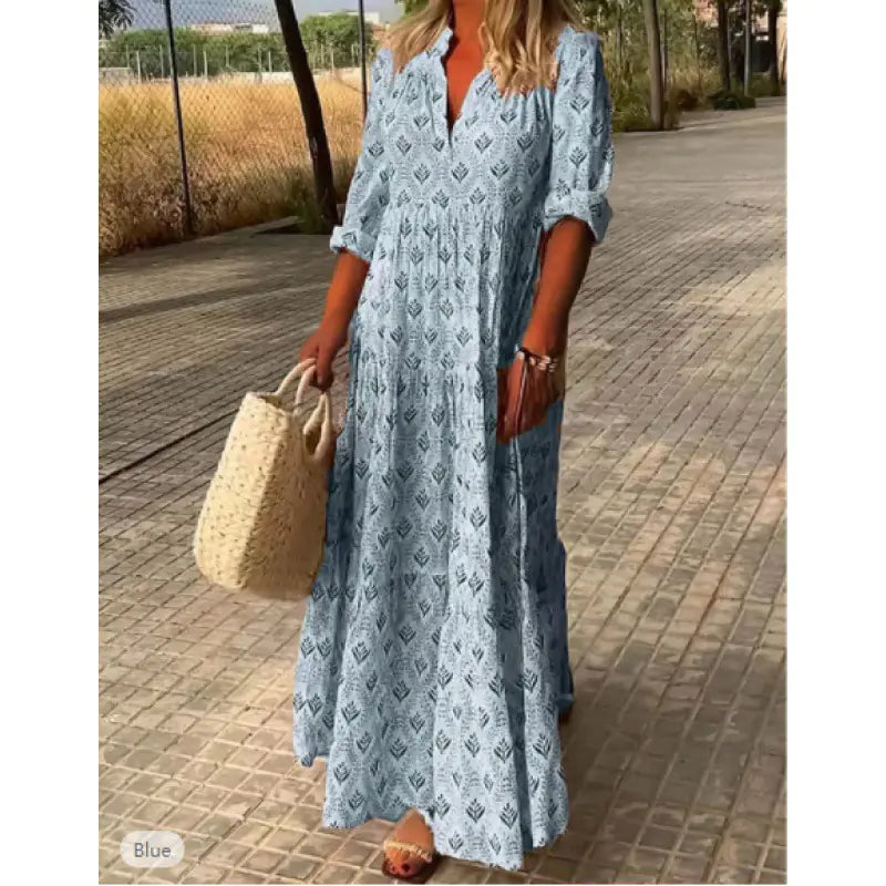 Woman wearing a blue patterned dress holding a straw bag on a paved path.