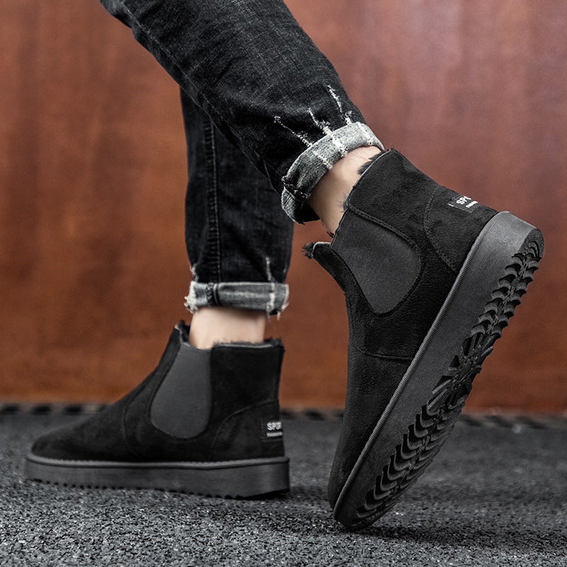 Black suede Chelsea boots worn with black jeans on a blurred background