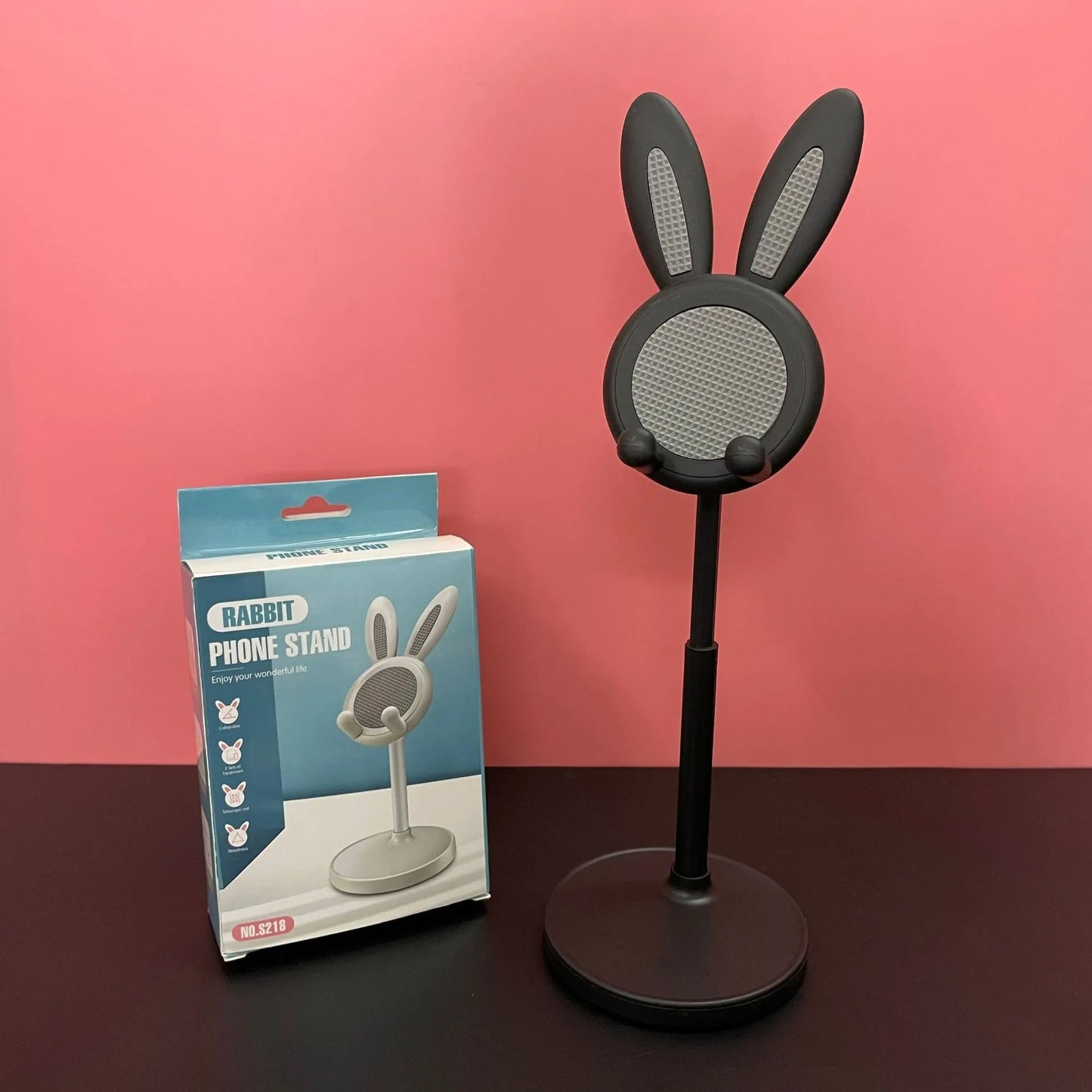 Black rabbit-shaped phone stand with packaging on a pink background