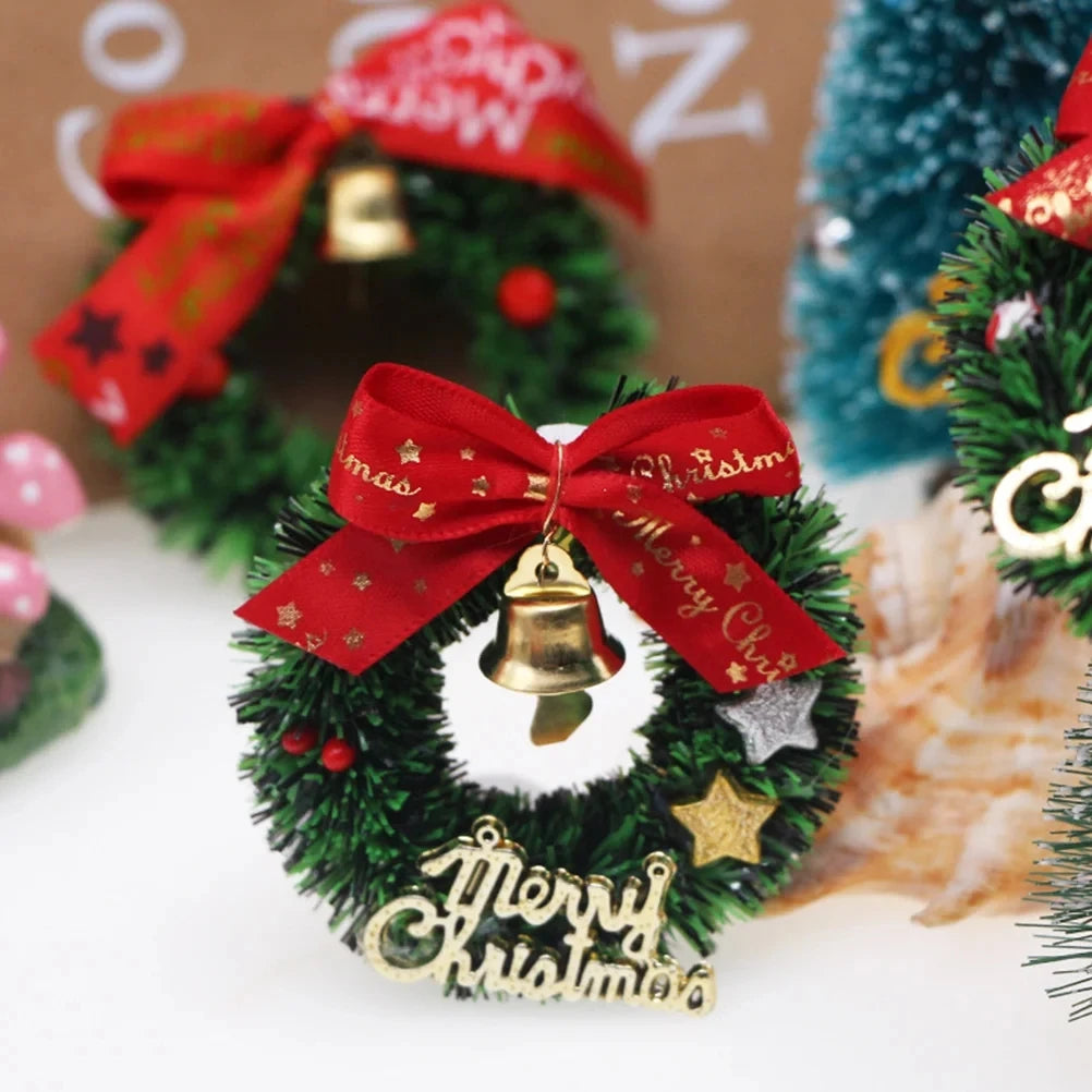 Small Christmas wreath ornament with a red bow and gold bell on a blurred background of more ornaments.