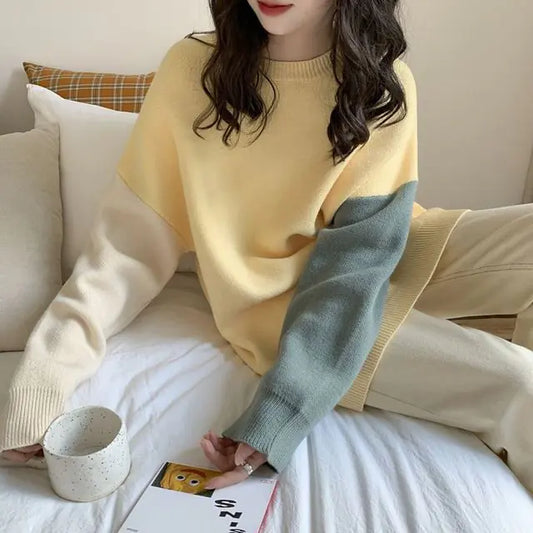 Person wearing a yellow sweater with a green sleeve, sitting on a couch holding a cup.