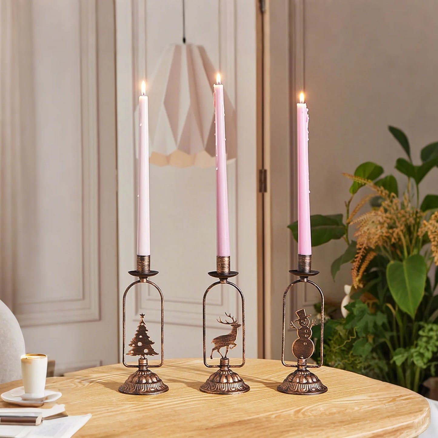 Three decorative candle holders with lit pink candles on a wooden table.