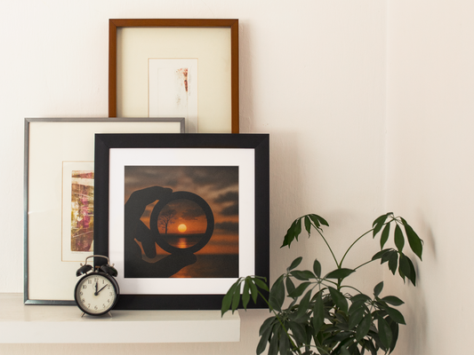 Framed sunset lens art print on a white shelf, styled with modern wall art, a plant, and a vintage alarm clock.