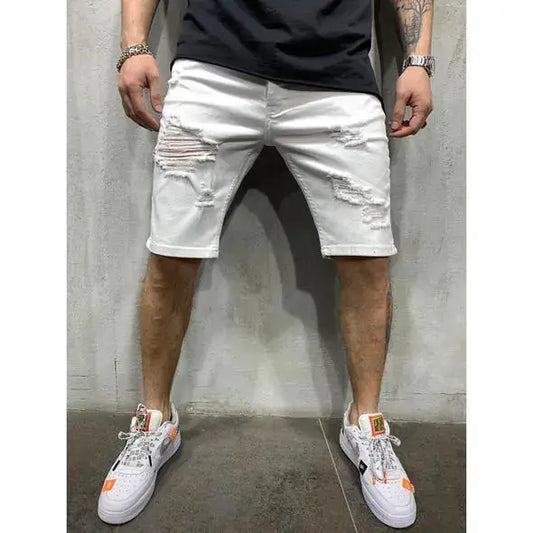 Person wearing white distressed denim shorts and white sneakers against a concrete wall.