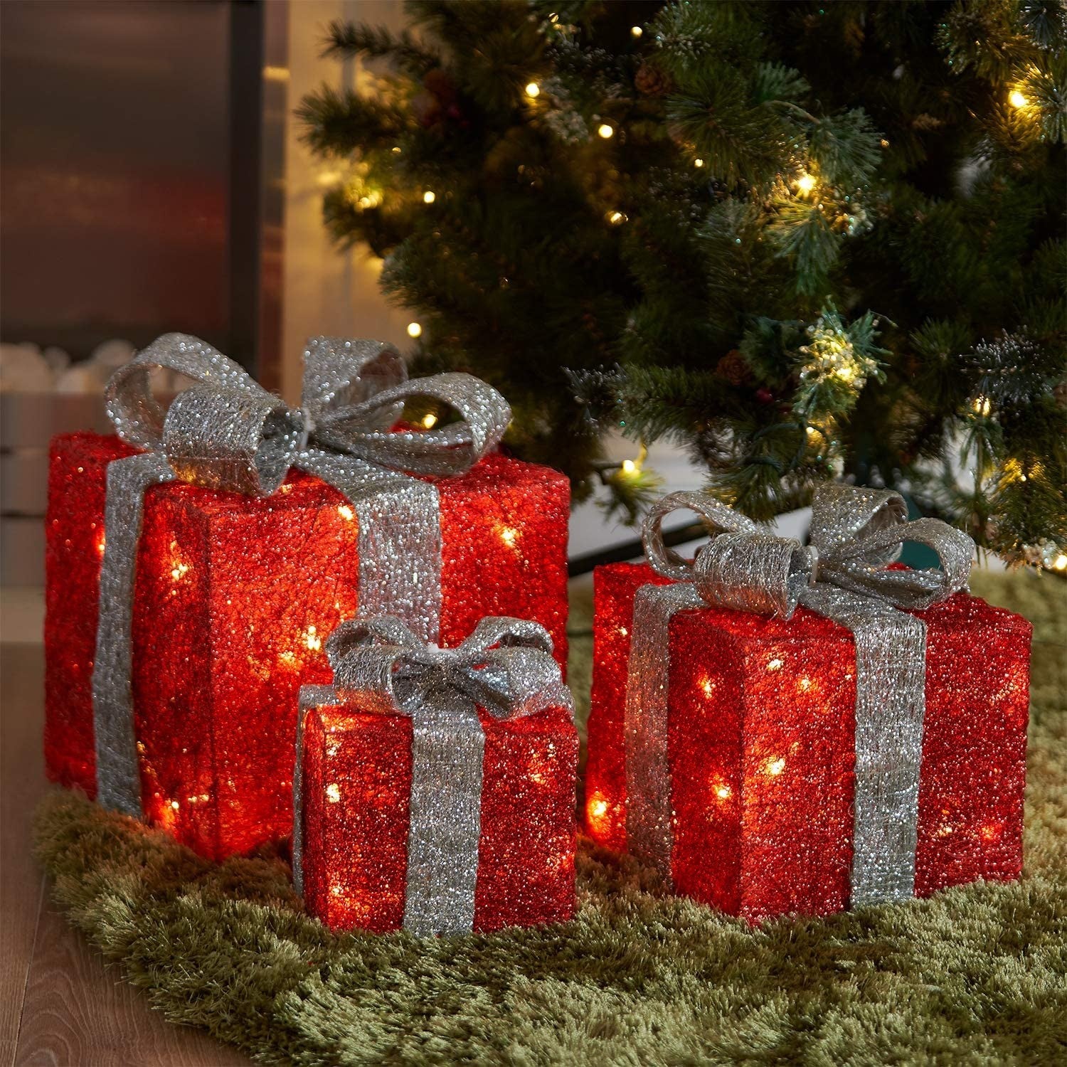 Set of 3 red and silver LED Christmas gift box decorations glowing under a Christmas tree