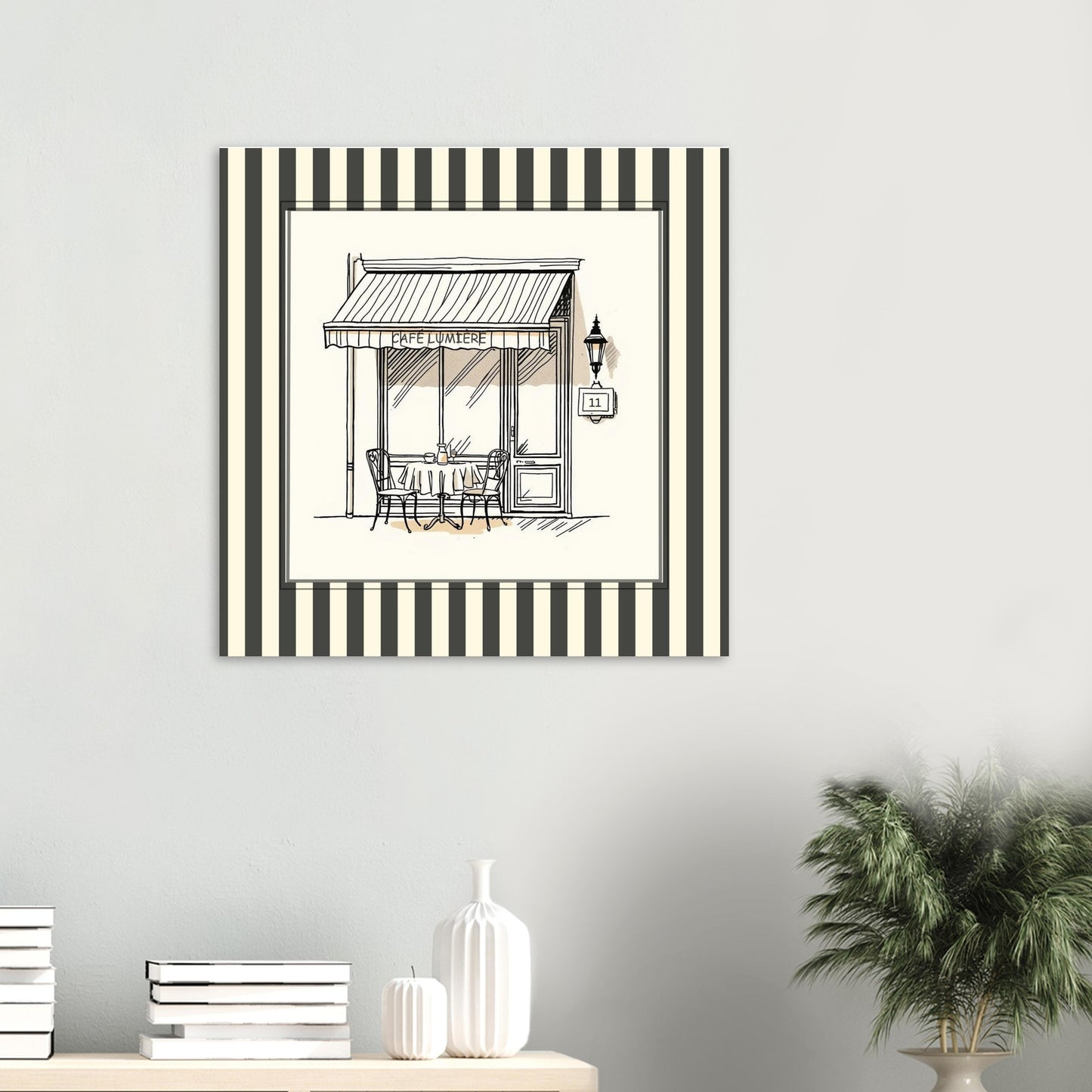 Black and cream Paris café art print displayed on a green wall above a sideboard with white ornaments and some books