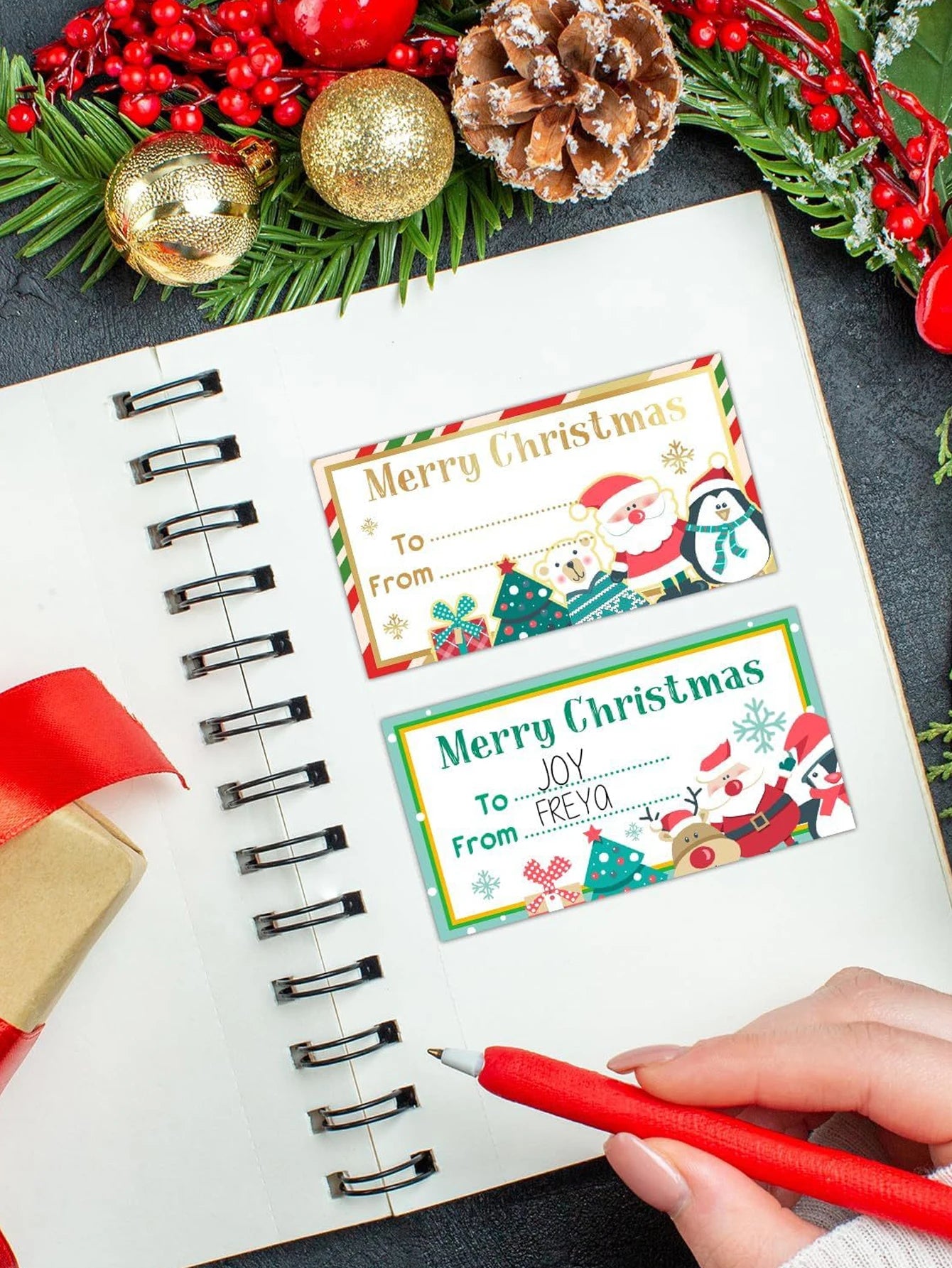Christmas gift tags with Santa Claus and penguins on a notebook with festive decorations.