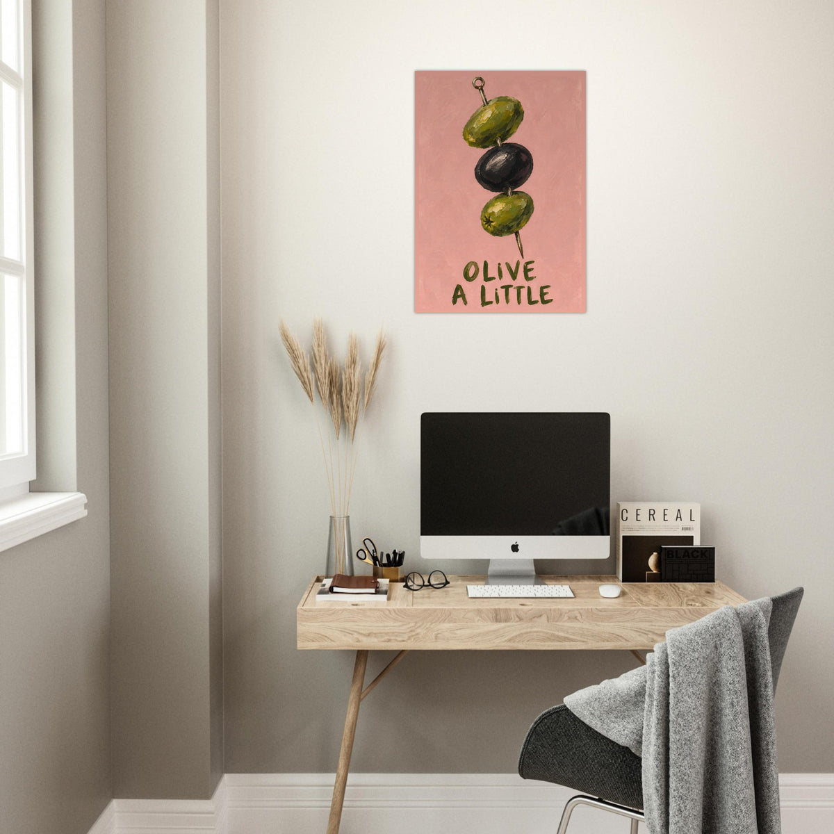 Olive a Little print above a wooden desk with a computer, beside a window in a softly lit home office.