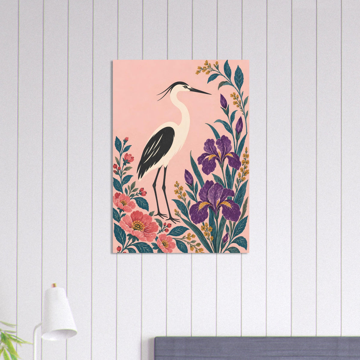 A vertical canvas wall art print featuring a heron bird and purple irises on a soft pink background, styled on a white wood-paneled wall above a bed.